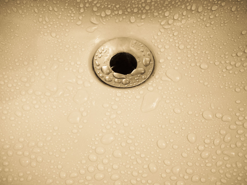 Close-up of a sink drain with water droplets on the basin