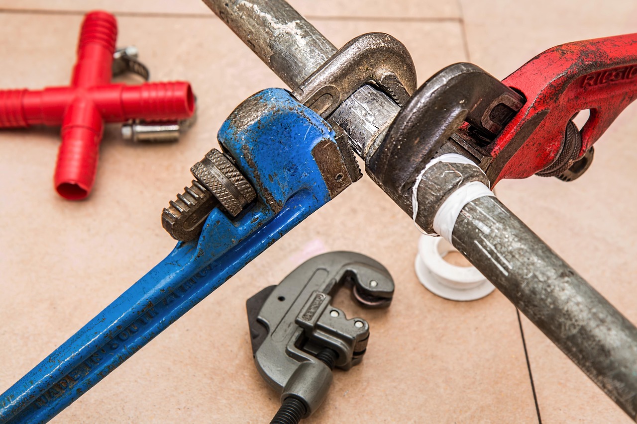 Pipe wrenches, cutter and plumbing fittings on a tiled floor